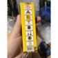 Image d’une boîte jaune présentant plusieurs logos de certifications thaïlandaises, dont des labels de qualité, des marques officielles, des distinctions OTOP et des trophées. La main tient le produit pour montrer ses garanties d’authenticité et de conformité.