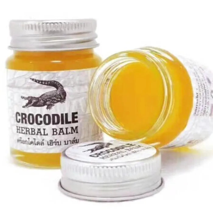 Deux pots de Crocodile Herbal Balm, dont un ouvert révélant un baume jaune. Baume traditionnel utilisé pour apaiser irritations, douleurs légères et inconforts cutanés. Packaging avec crocodile, évoquant un soin puissant et protecteur.